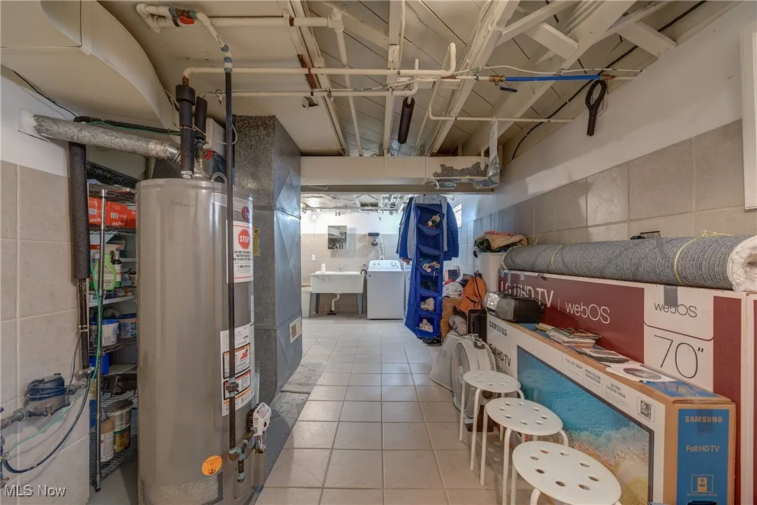 Unfinished below grade area featuring tile walls, water heater, washer / dryer, and tile patterned floors