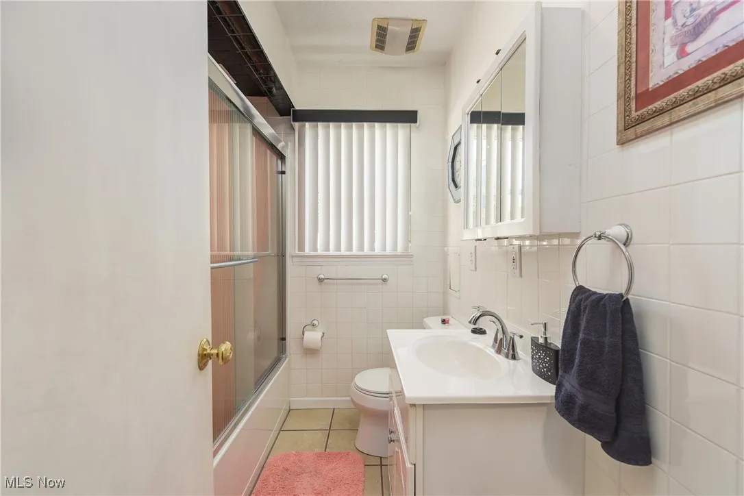 Full bath with vanity, tile walls, tile patterned flooring, and shower / bath combination with glass door