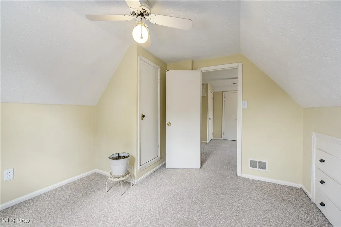 Additional living space with a textured ceiling, carpet flooring, vaulted ceiling, and a ceiling fan