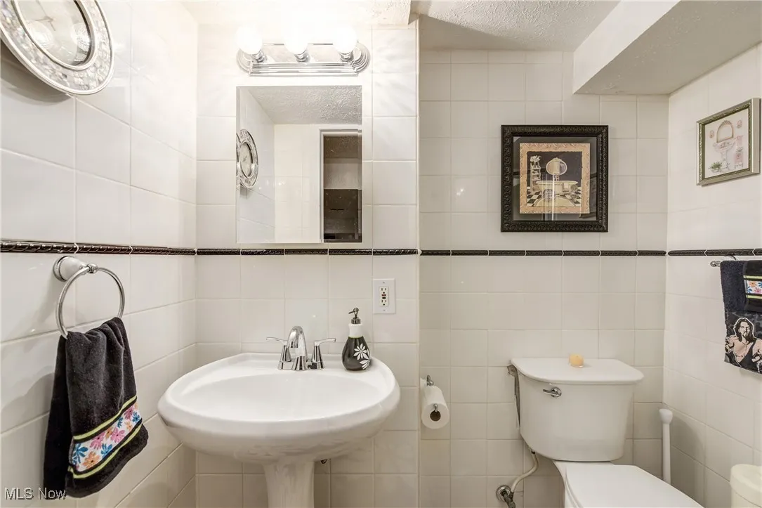 Half bathroom with a textured ceiling and tile walls