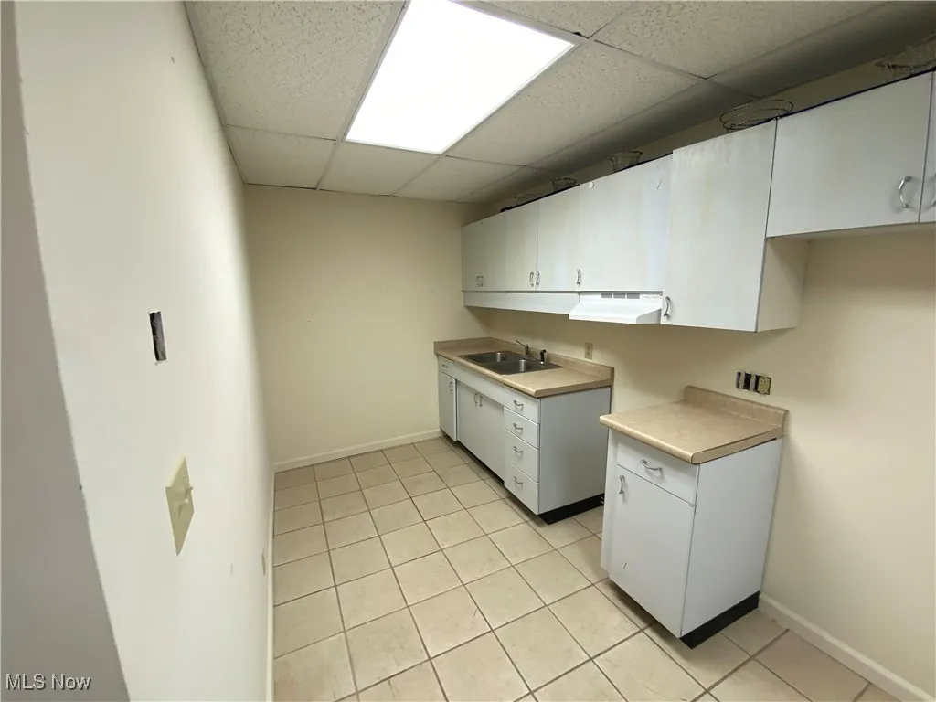 Kitchen featuring sink, white cabinetry, light tile patterned flooring, and a drop ceiling