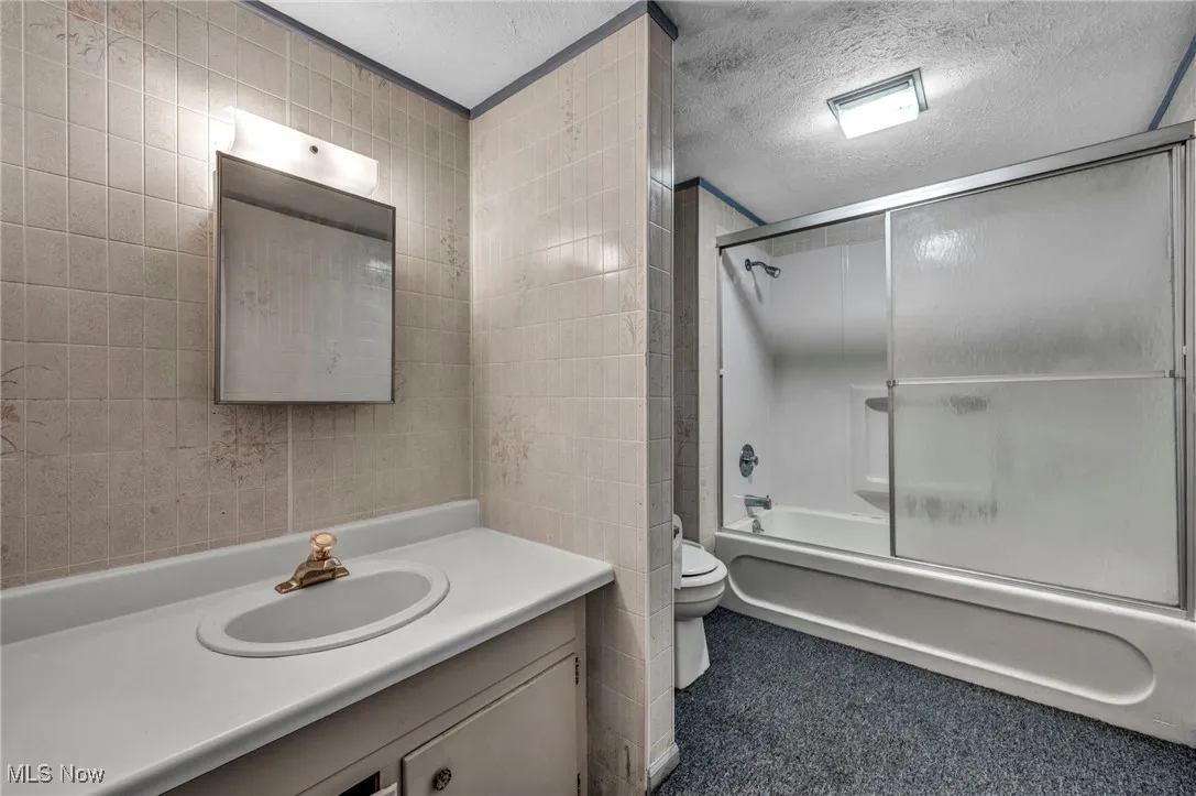 Bathroom with tile walls, a textured ceiling, enclosed tub / shower combo, and vanity