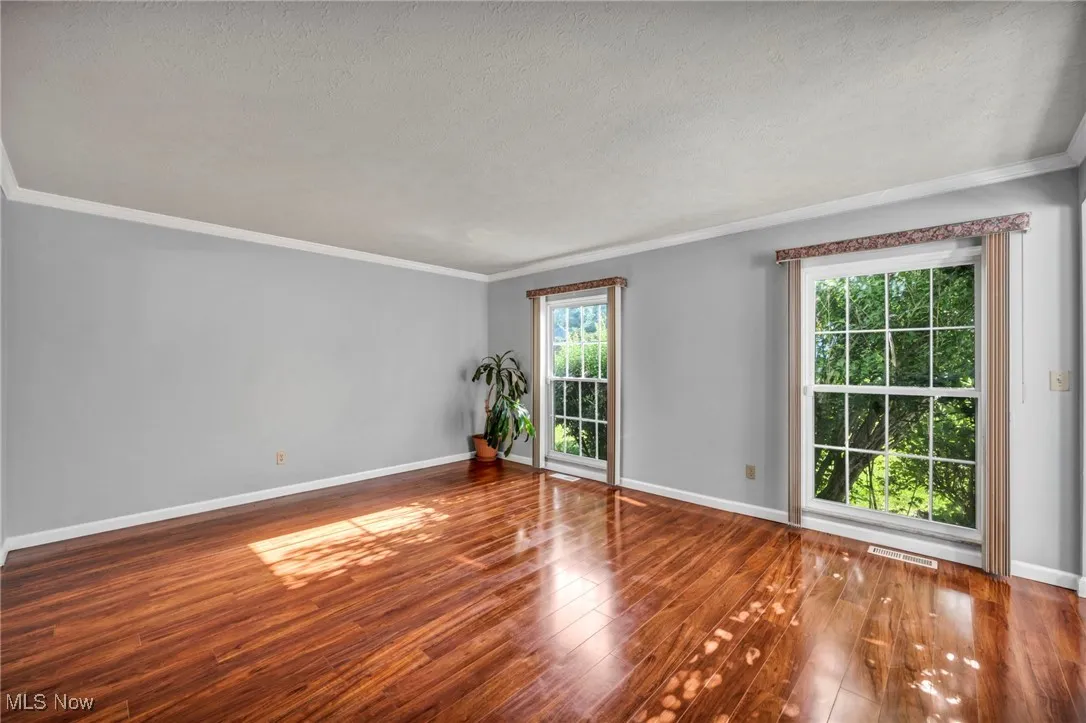 Empty room featuring wood finished floors, crown molding, and a textured ceiling