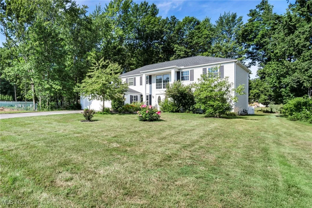 Colonial house featuring driveway, a front lawn, a garage, and view of scattered trees