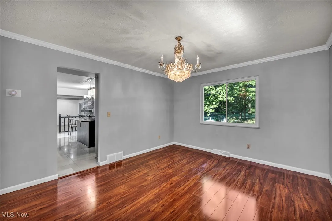 Empty room with a chandelier, ornamental molding, wood finished floors, and a textured ceiling
