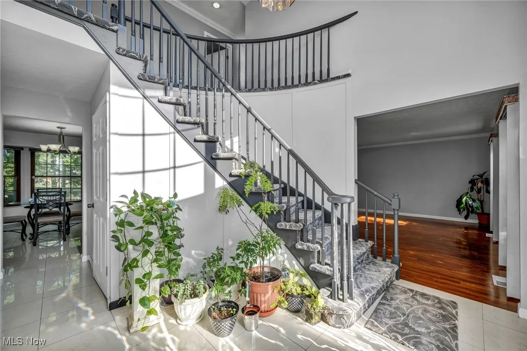 Staircase with a chandelier, tile patterned flooring, a high ceiling, and crown molding