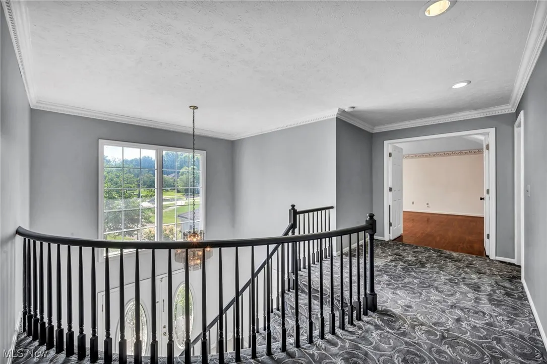 Corridor with an upstairs landing, ornamental molding, a textured ceiling, a chandelier, and carpet