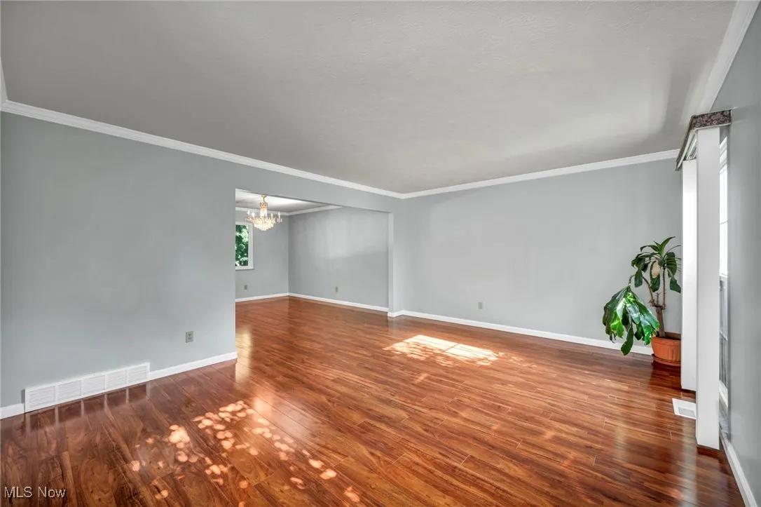 Spare room with a chandelier, wood finished floors, and crown molding