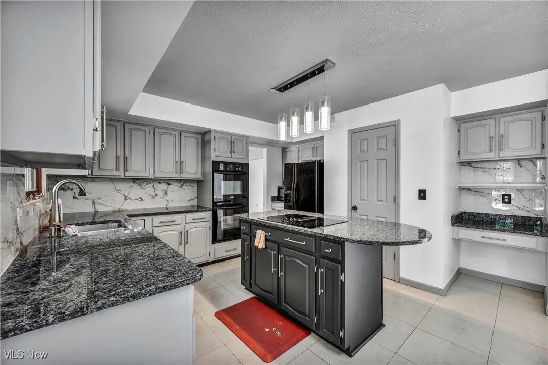 Kitchen featuring backsplash, dark stone counters, black appliances, a textured ceiling, and pendant lighting