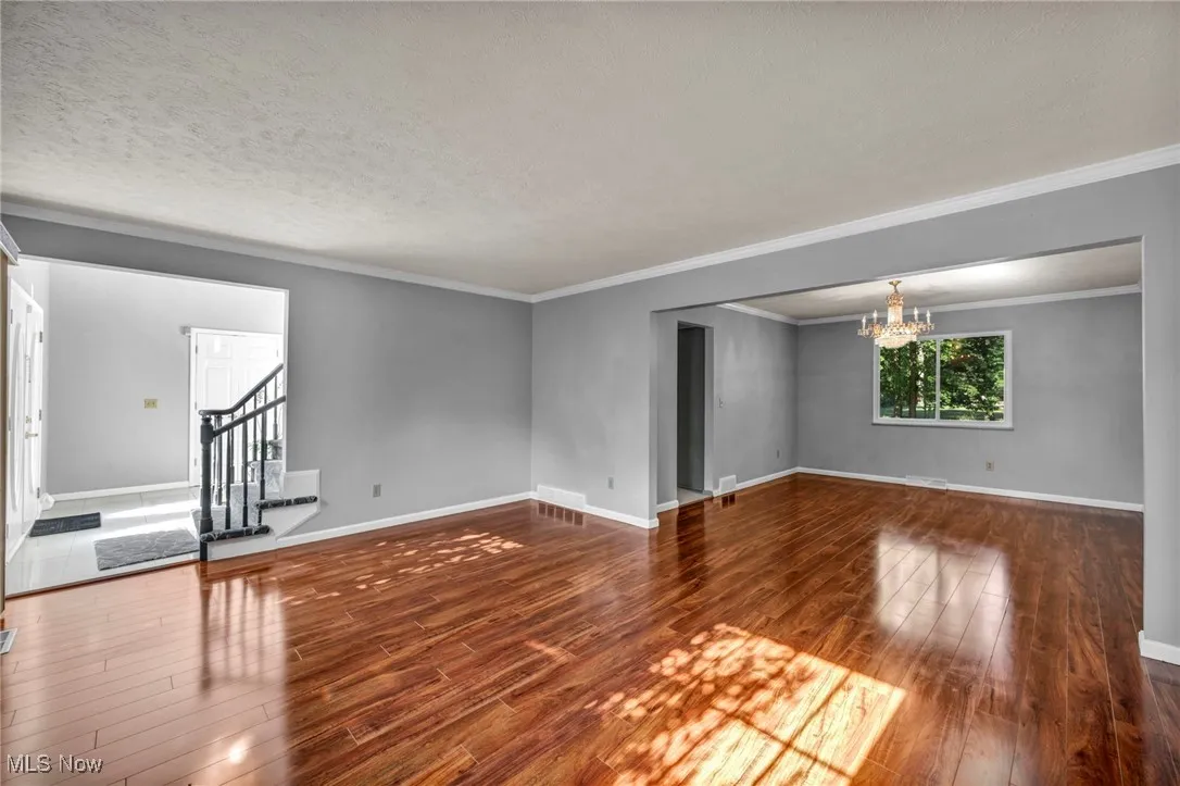 Unfurnished room with hardwood / wood-style flooring, a chandelier, stairway, crown molding, and a textured ceiling