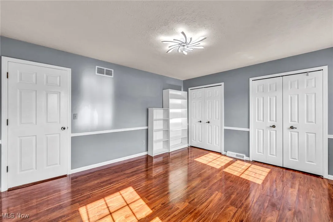 Unfurnished bedroom featuring multiple closets, wood finished floors, and a textured ceiling