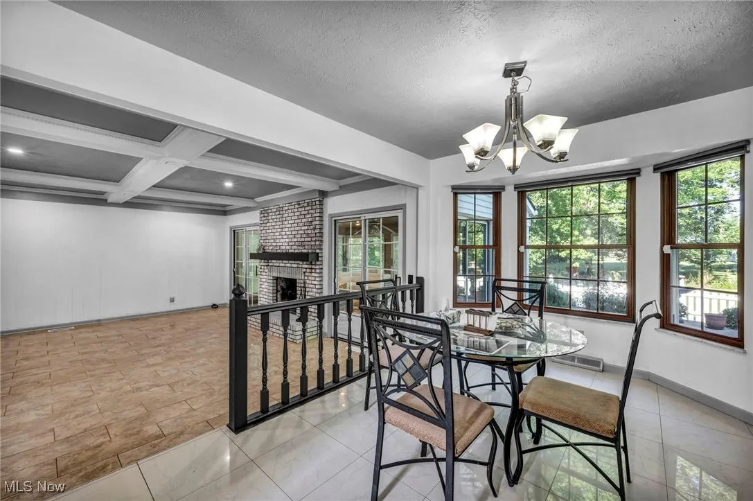 Dining room with beam ceiling, a chandelier, coffered ceiling, a brick fireplace, and recessed lighting