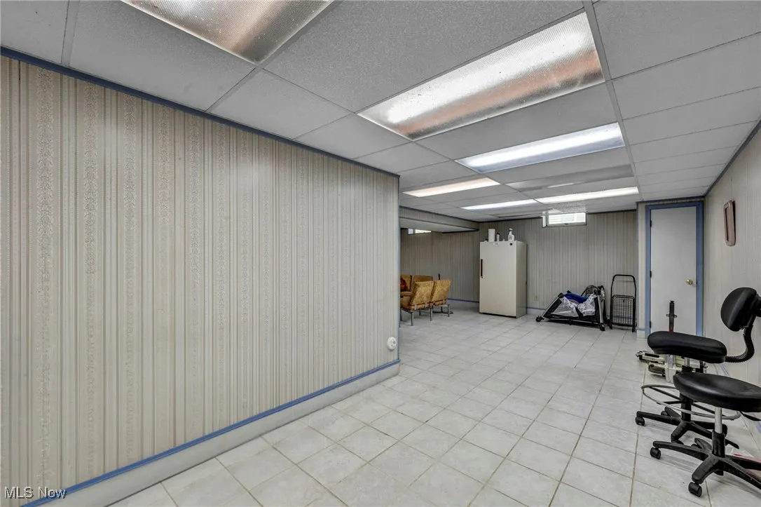Basement with a paneled ceiling, freestanding refrigerator, and tile patterned floors