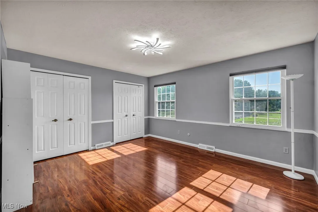 Unfurnished bedroom featuring wood-type flooring, two closets, and a textured ceiling