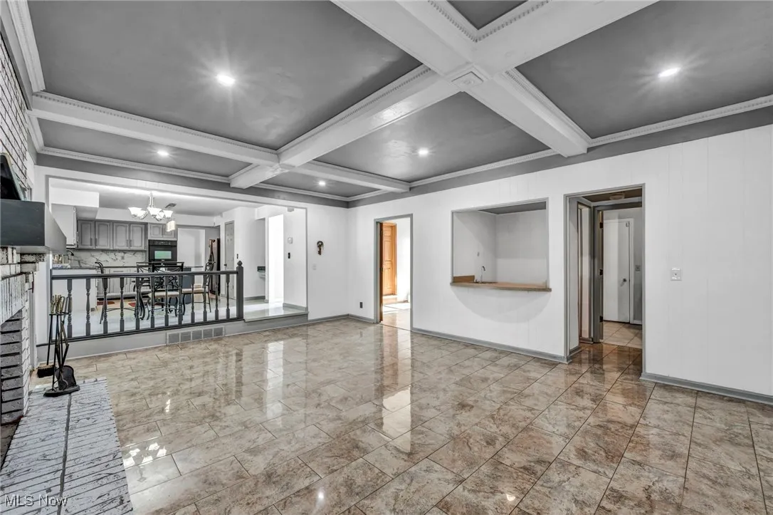 Empty room featuring recessed lighting, a brick fireplace, beam ceiling, a chandelier, and coffered ceiling