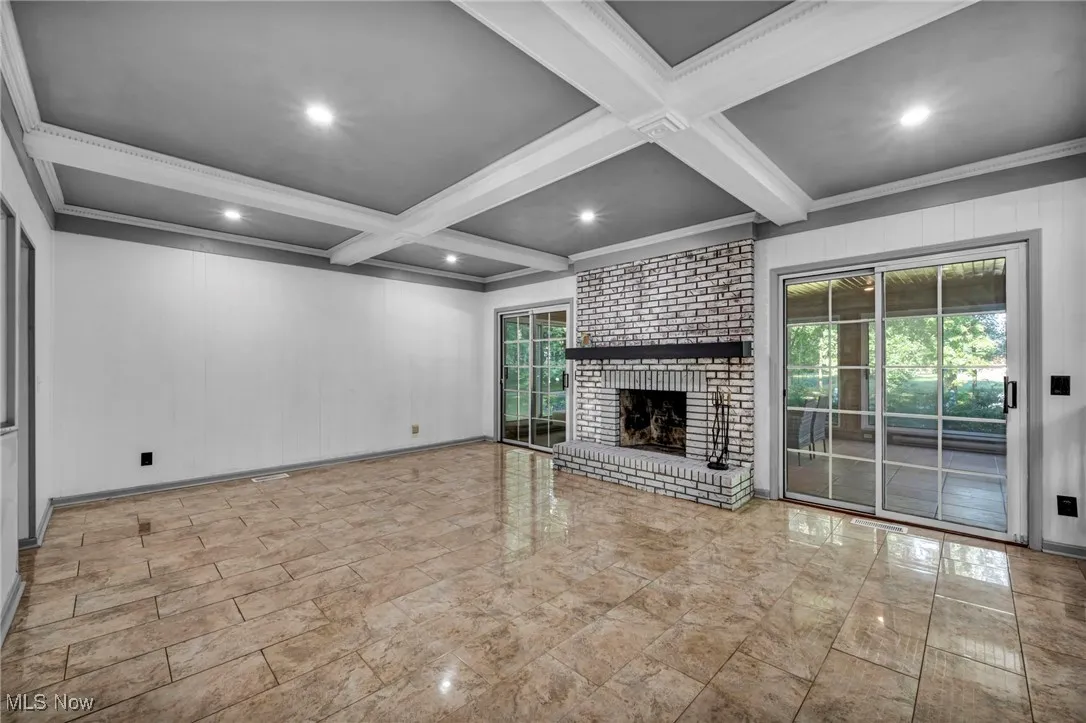 Unfurnished living room featuring beamed ceiling, ornamental molding, coffered ceiling, recessed lighting, and a brick fireplace