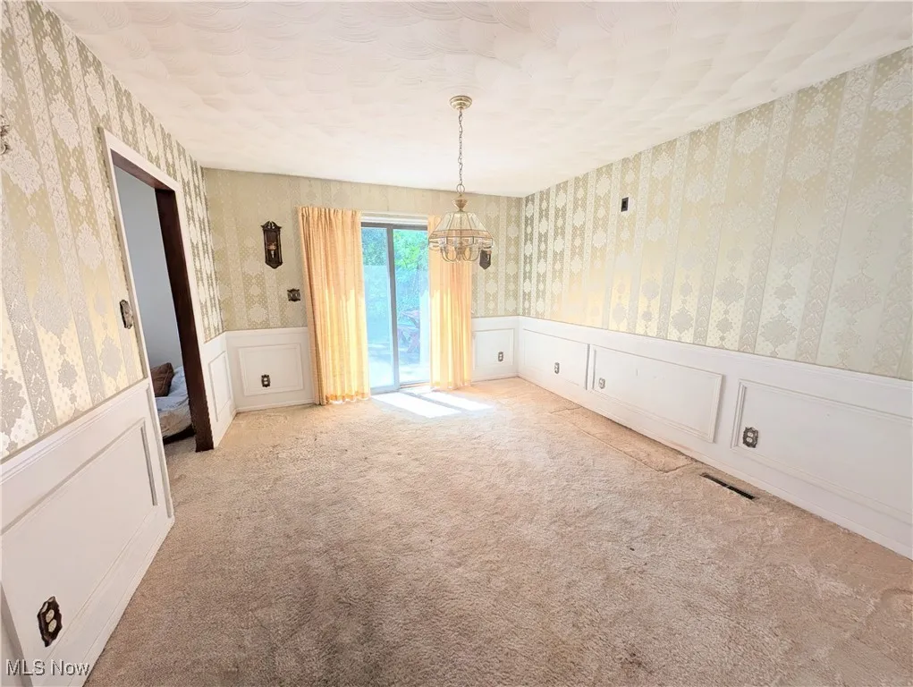 Spare room featuring wallpapered walls, a decorative wall, a textured ceiling, a chandelier, and wainscoting