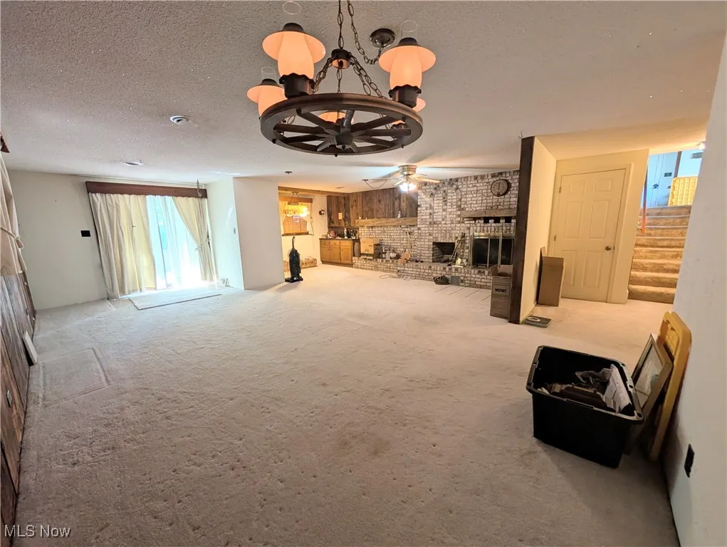Unfurnished living room with carpet flooring, a chandelier, stairs, a textured ceiling, and a fireplace