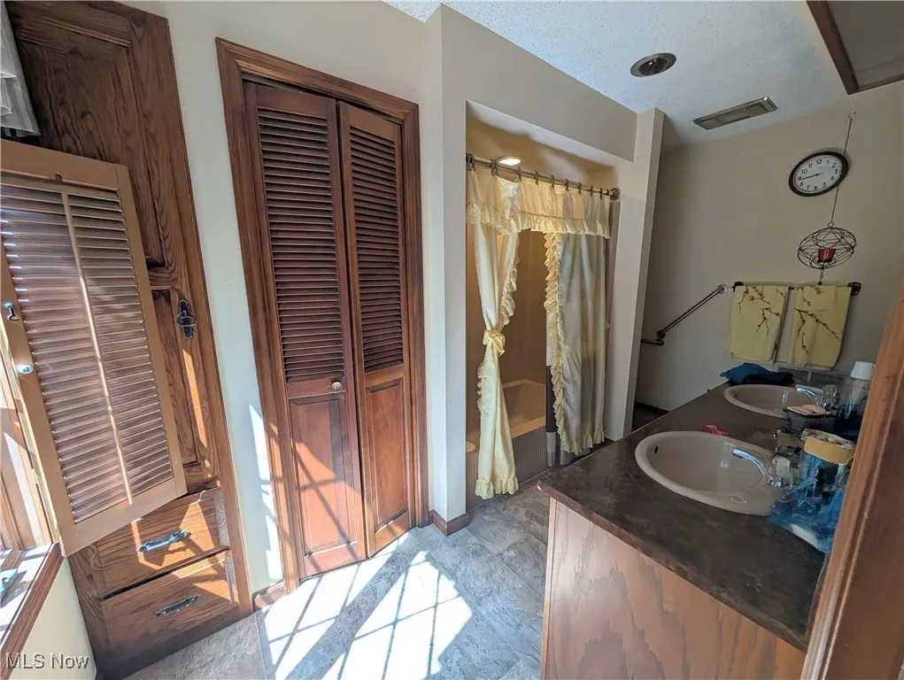 Full bathroom featuring a closet, double vanity, a textured ceiling, and a heating unit