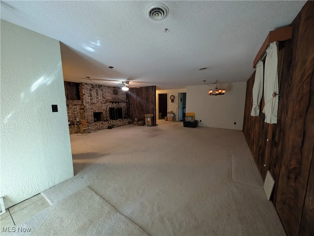 Unfurnished living room featuring carpet floors, a fireplace, a ceiling fan, a textured ceiling, and a chandelier