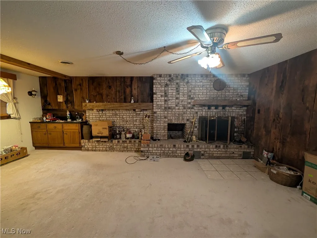 Unfurnished living room featuring wood walls, a textured ceiling, ceiling fan, and a brick fireplace