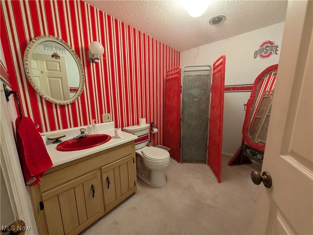 Bathroom featuring a textured ceiling, vanity, and wallpapered walls