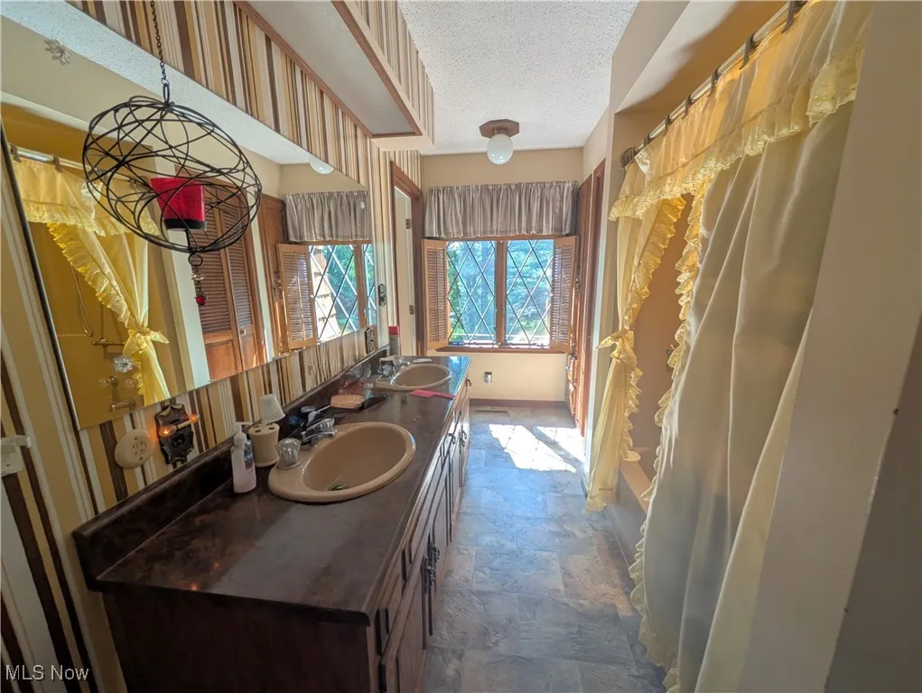 Full bathroom with double vanity, stone finish flooring, and a textured ceiling