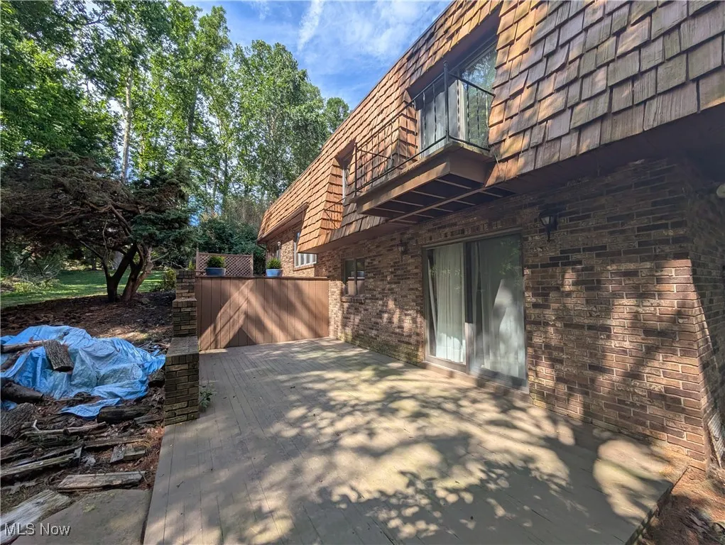 View of property exterior featuring mansard roof, brick siding, a balcony, and a patio area