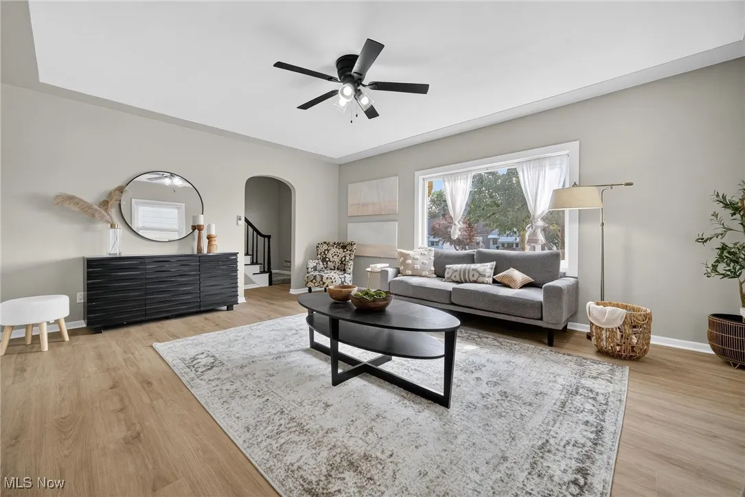 Living area with arched walkways, ceiling fan, light wood-style floors, and stairs