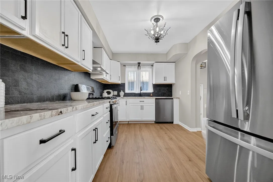 Kitchen with appliances with stainless steel finishes, a chandelier, backsplash, light wood finished floors, and white cabinets