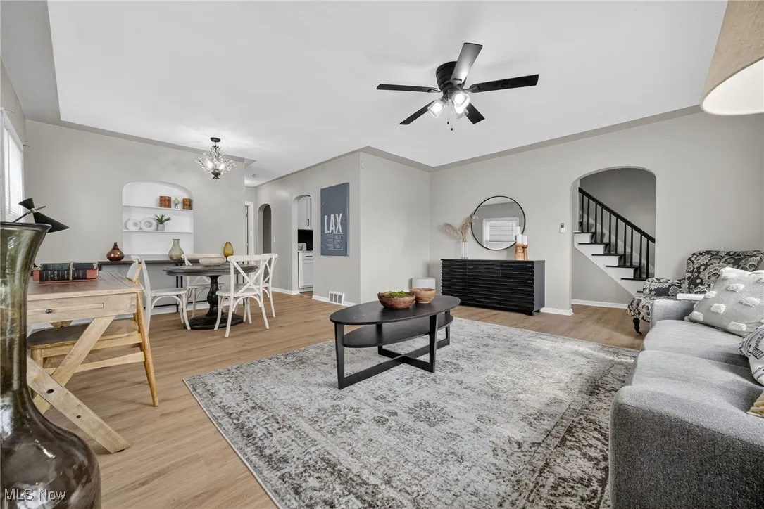 Living area with arched walkways, a ceiling fan, light wood finished floors, stairs, and a chandelier