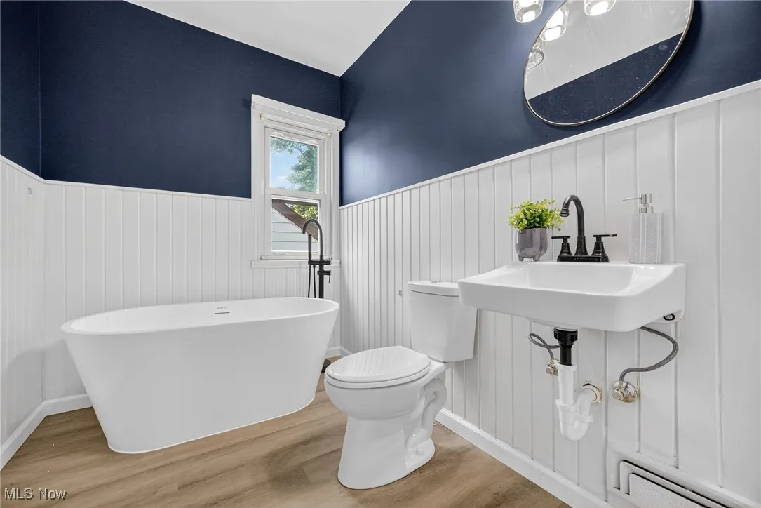 Bathroom with a wainscoted wall, a freestanding tub, wood finished floors, and a baseboard radiator