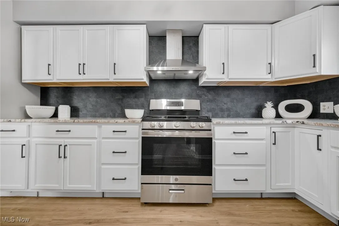 Kitchen featuring stainless steel gas range, wall chimney range hood, and white cabinets