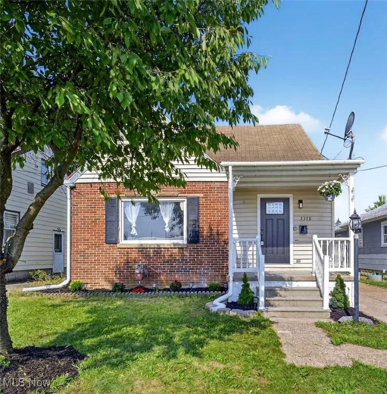 View of front facade with covered porch, a front yard, brick siding, and roof with shingles