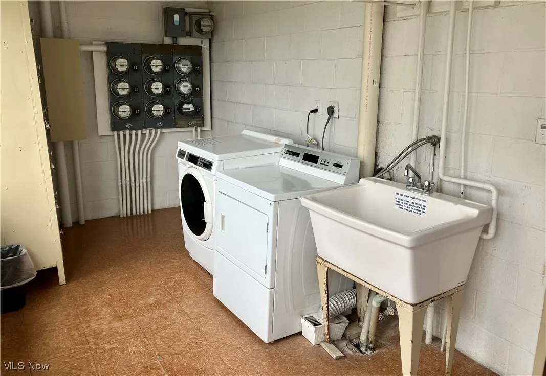 Washroom featuring washer and clothes dryer, concrete block wall, and light floors