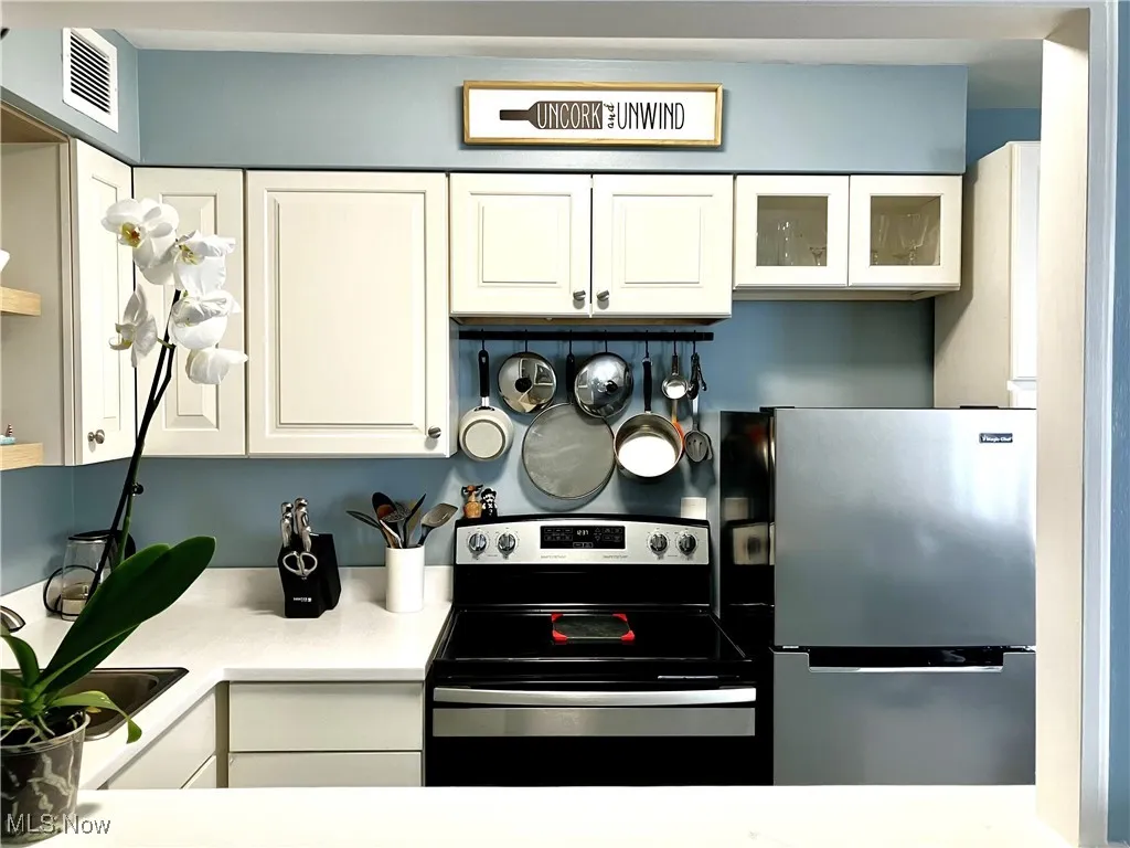 Kitchen with stainless steel appliances, white cabinets, glass insert cabinets, and light countertops