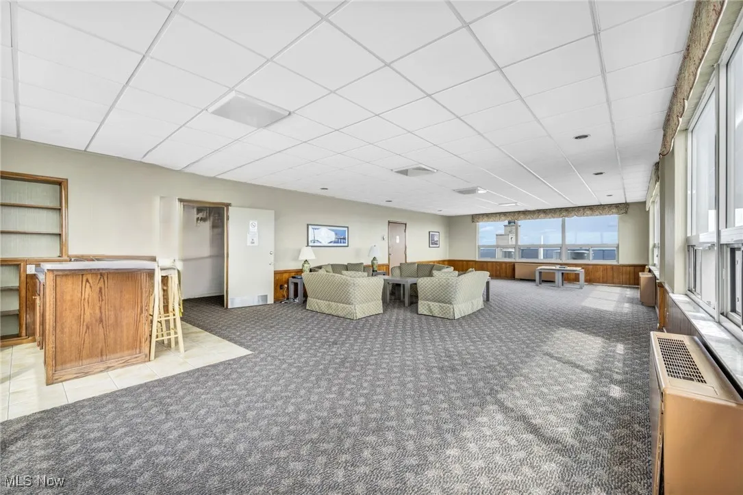 Living room with a paneled ceiling, light colored carpet, and a dry bar
