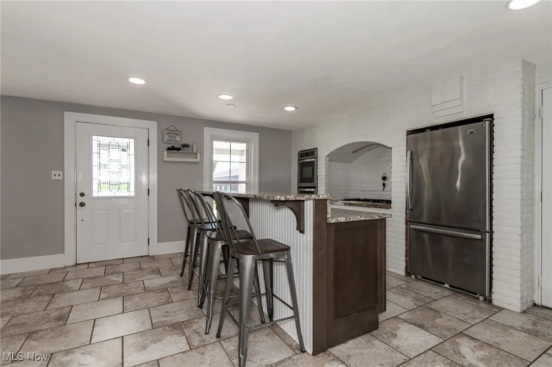 Kitchen with freestanding refrigerator, a kitchen breakfast bar, recessed lighting, and light stone counters