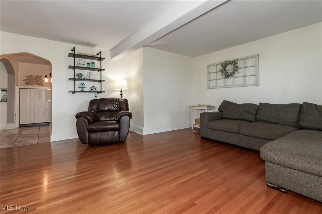 Living area with arched walkways, light wood-style floors, and beamed ceiling
