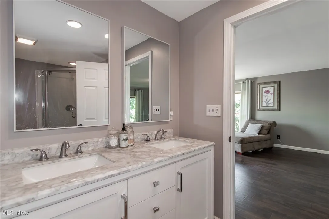 Ensuite bathroom featuring healthy amount of natural light, double vanity, wood finished floors, and an enclosed shower