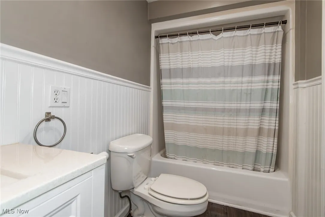 Bathroom featuring wainscoting, shower / bath combo, vanity, a decorative wall, and wood finished floors