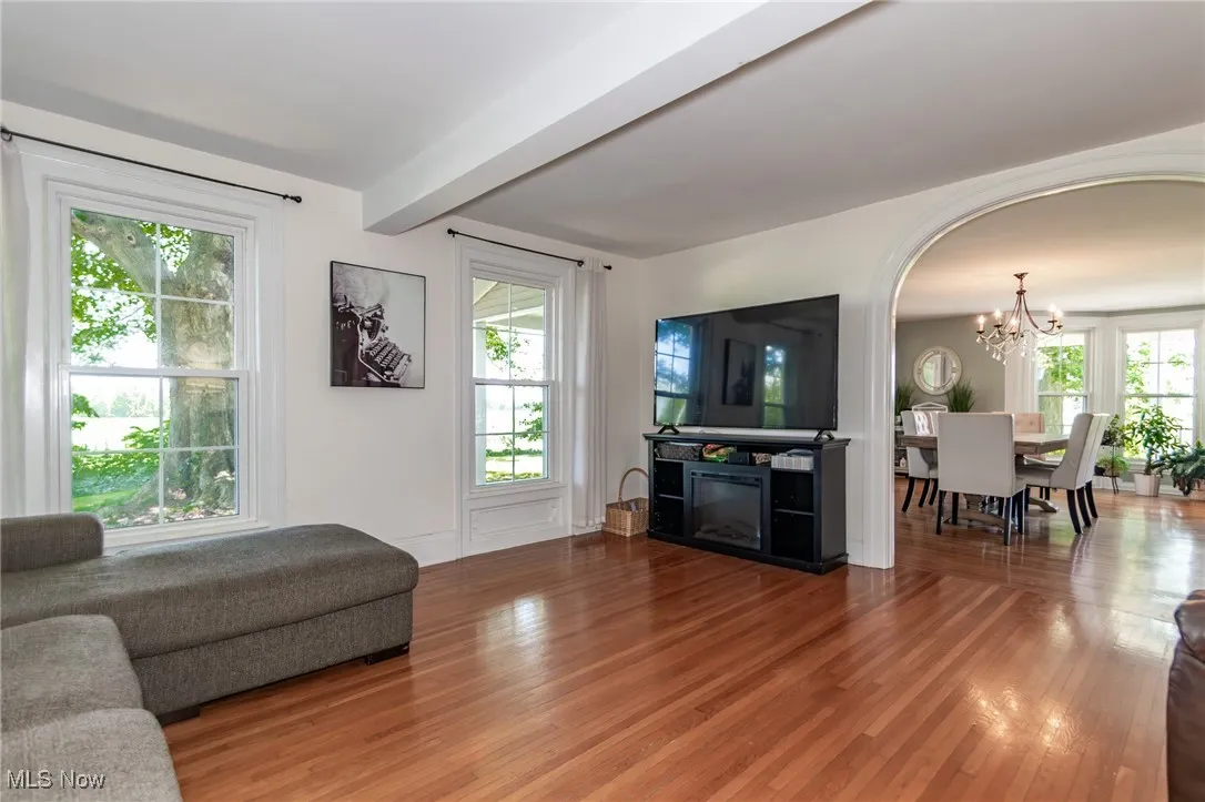 Living area with a chandelier, plenty of natural light, beam ceiling, arched walkways, and wood finished floors