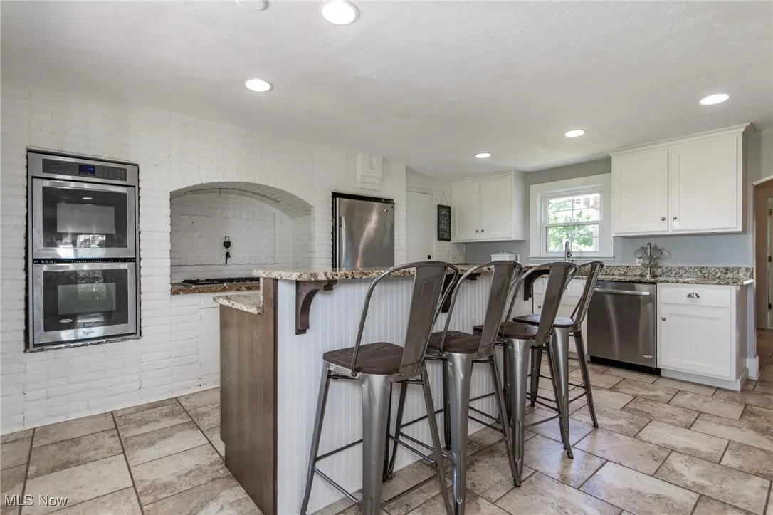 Kitchen with appliances with stainless steel finishes, a breakfast bar, stone counters, white cabinets, and recessed lighting