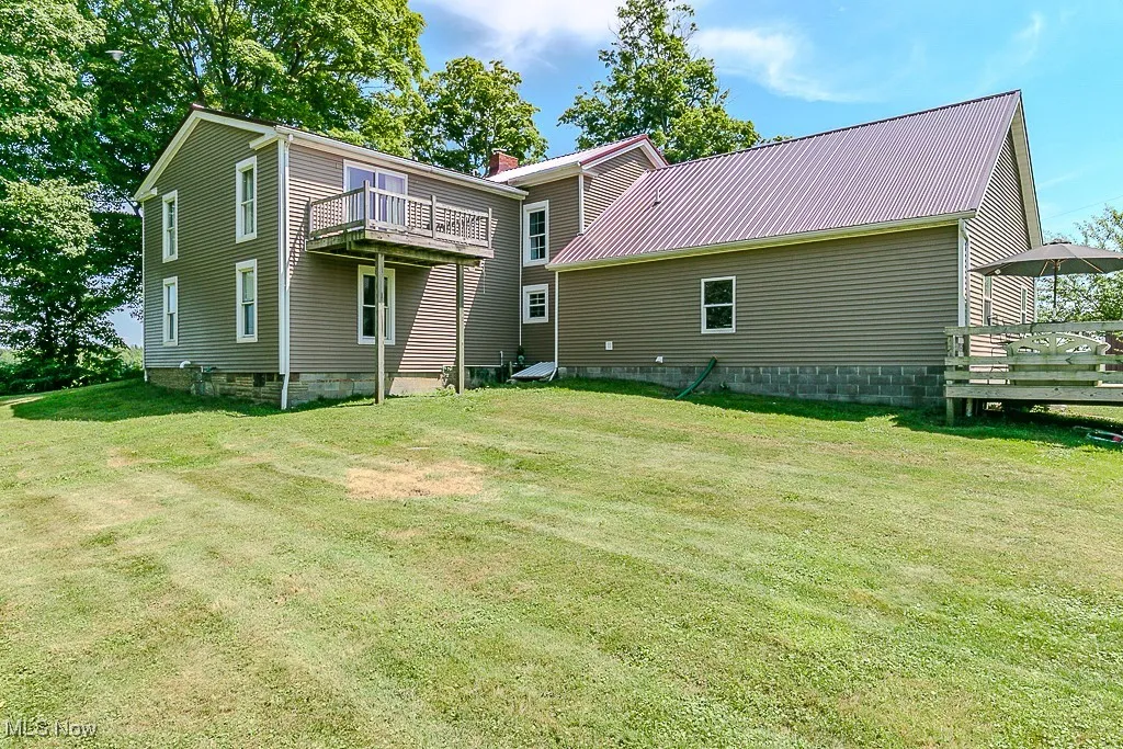 Rear view of property featuring a wooden deck, a yard, and a metal roof