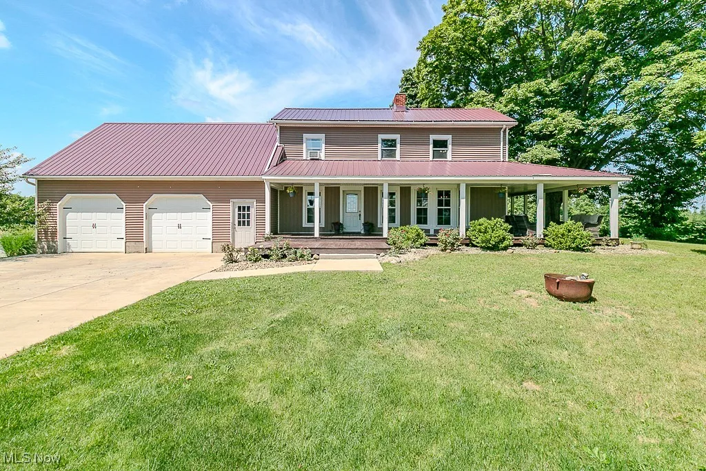 Farmhouse-style home with a porch, a metal roof, a garage, a chimney, and driveway