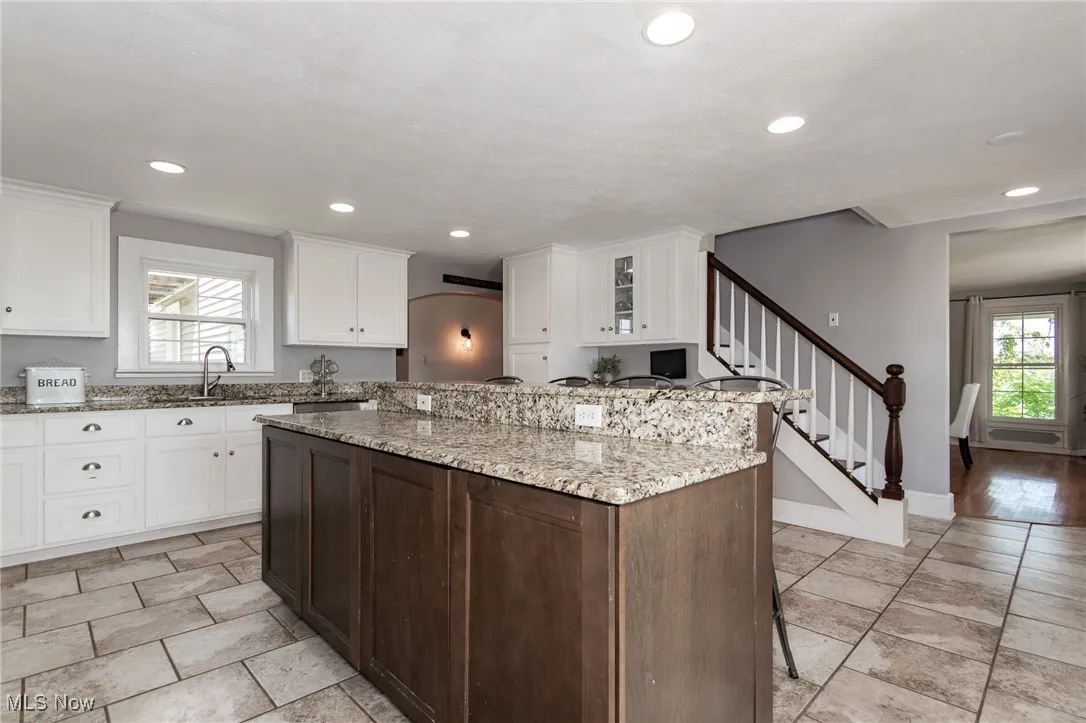 Kitchen featuring light stone countertops, white cabinetry, a kitchen island, recessed lighting, and a kitchen bar