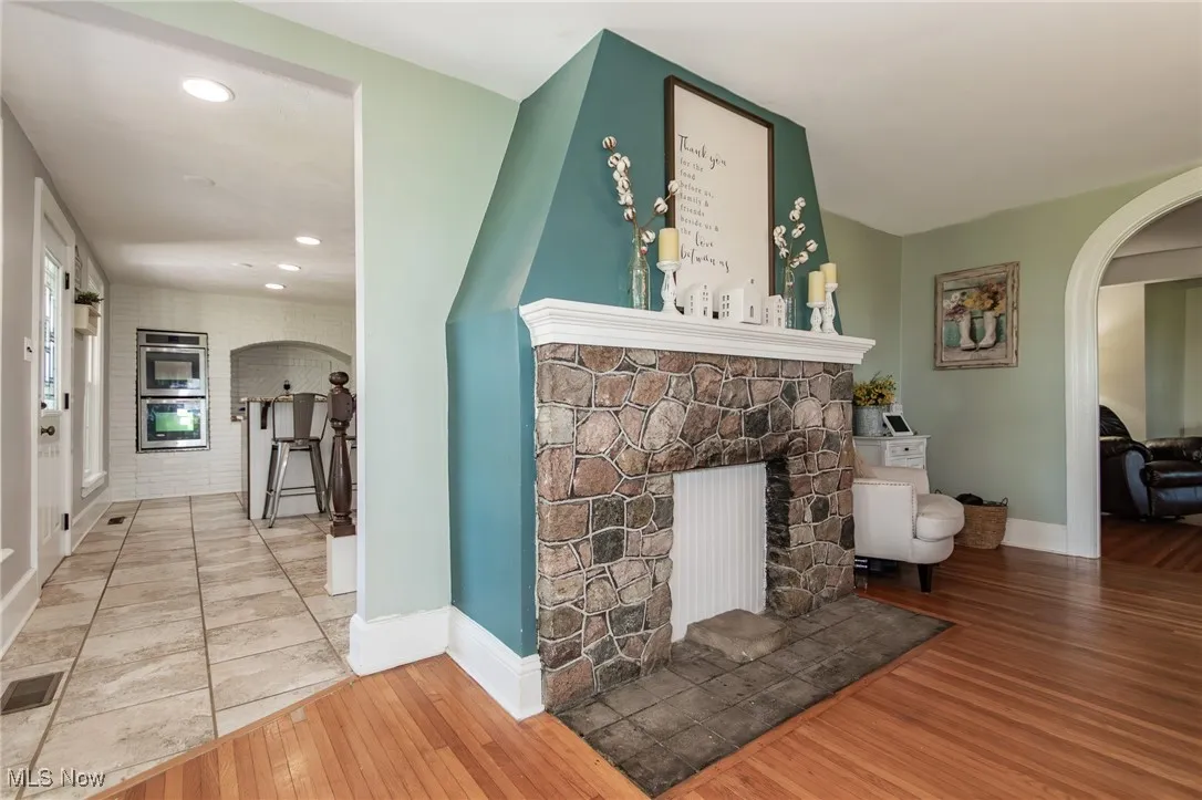 Living room featuring arched walkways, a stone fireplace, wood-type flooring, and recessed lighting