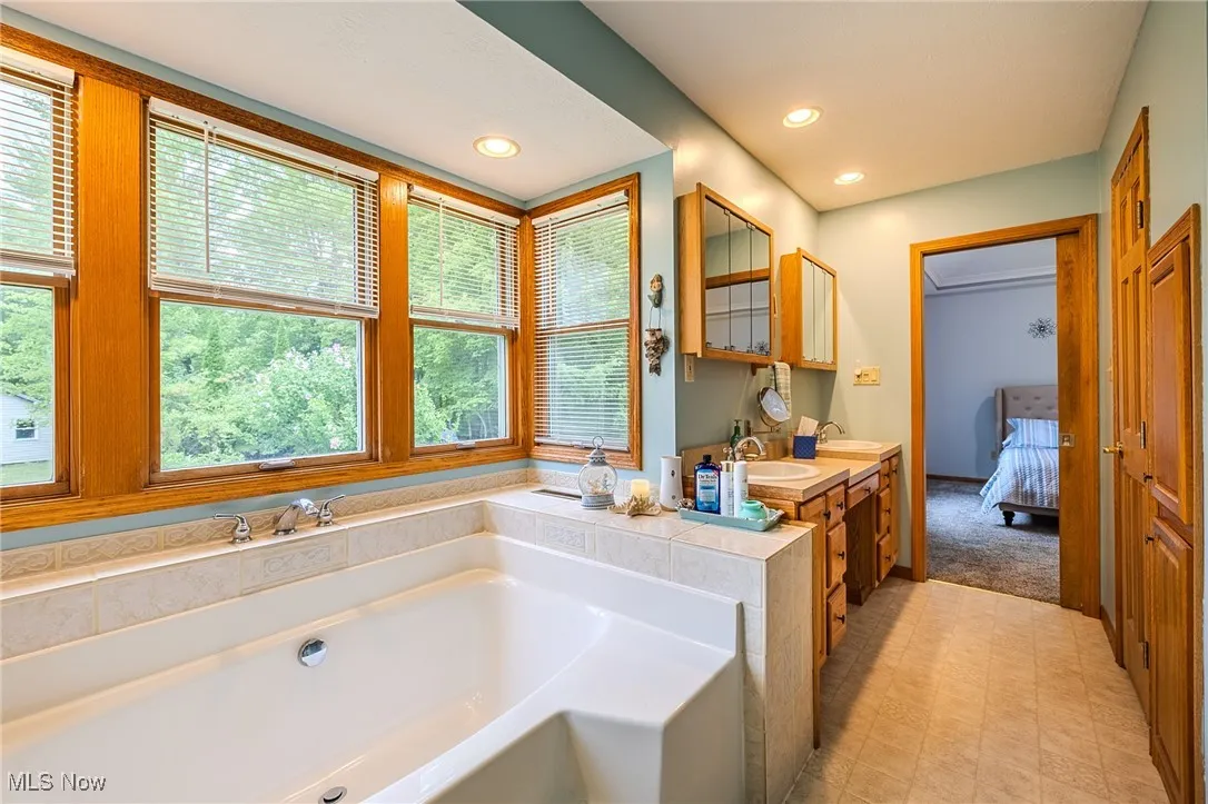 Ensuite bathroom featuring double vanity, a bath, recessed lighting, and tile patterned floors