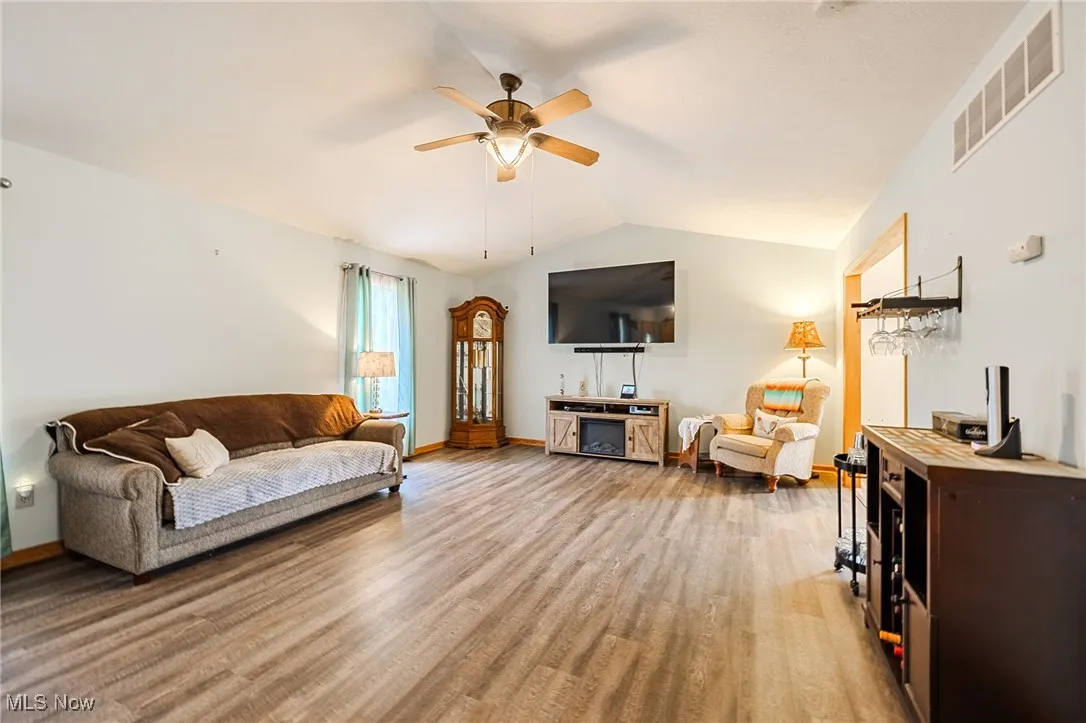Living room with light wood-style floors, a ceiling fan, and lofted ceiling