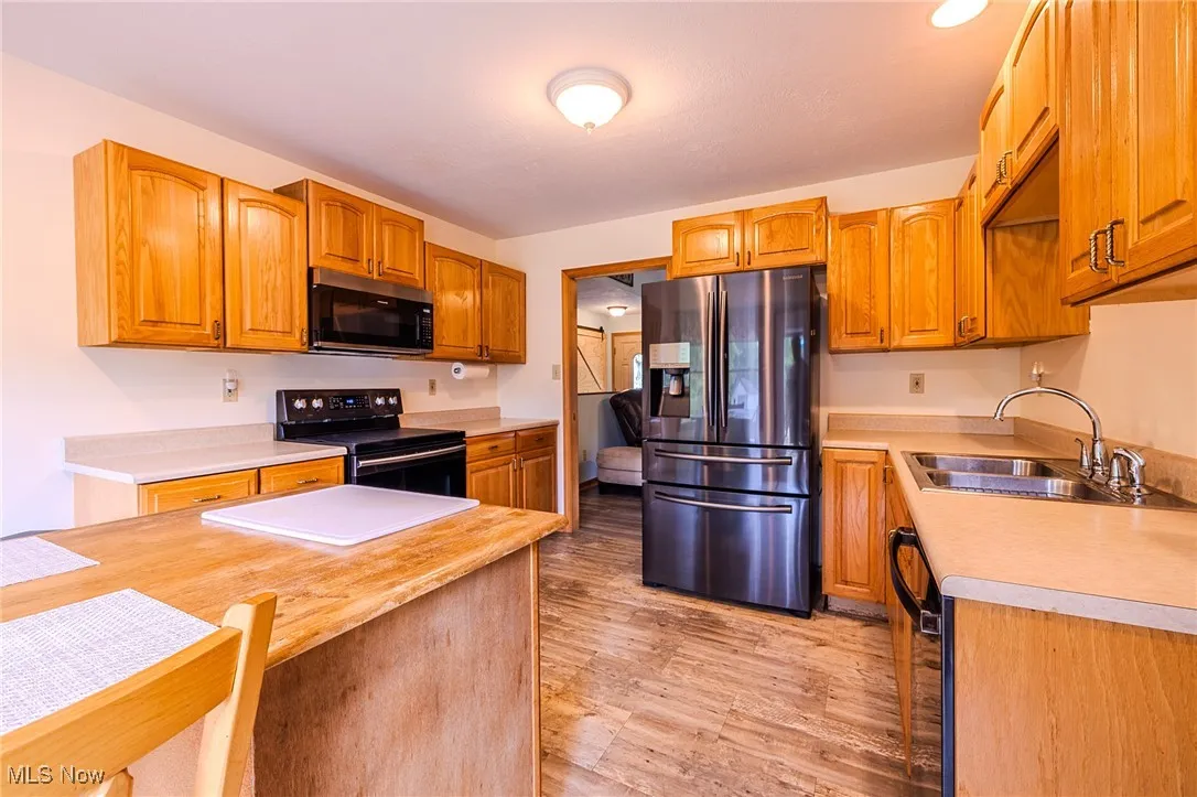 Kitchen featuring black appliances, light countertops, light wood-type flooring, and brown cabinets